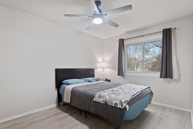 bedroom with ceiling fan, a textured ceiling, baseboards, and wood finished floors