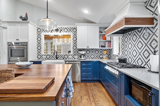 kitchen with blue cabinets, butcher block countertops, a sink, appliances with stainless steel finishes, and custom exhaust hood