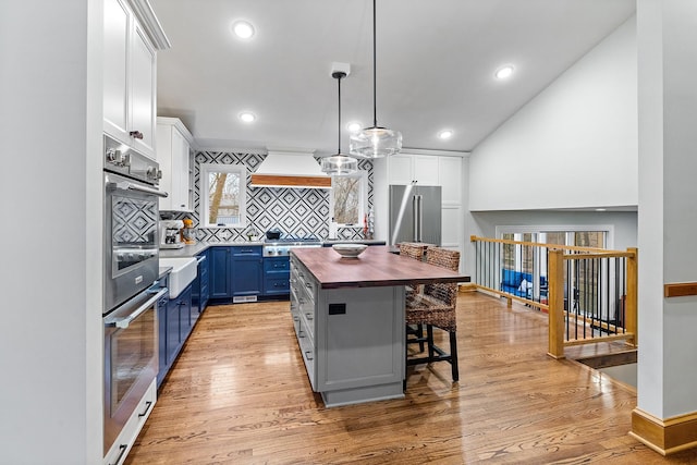 kitchen with blue cabinetry, custom exhaust hood, light wood-style floors, high quality fridge, and butcher block countertops