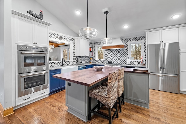 kitchen with blue cabinets, stainless steel appliances, wood counters, open shelves, and custom range hood