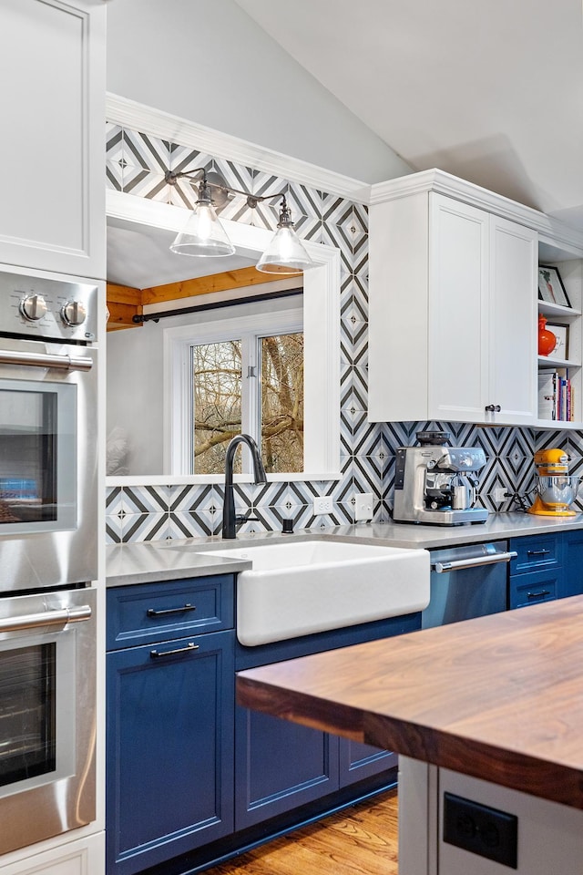 kitchen featuring stainless steel appliances, vaulted ceiling, wooden counters, blue cabinetry, and open shelves