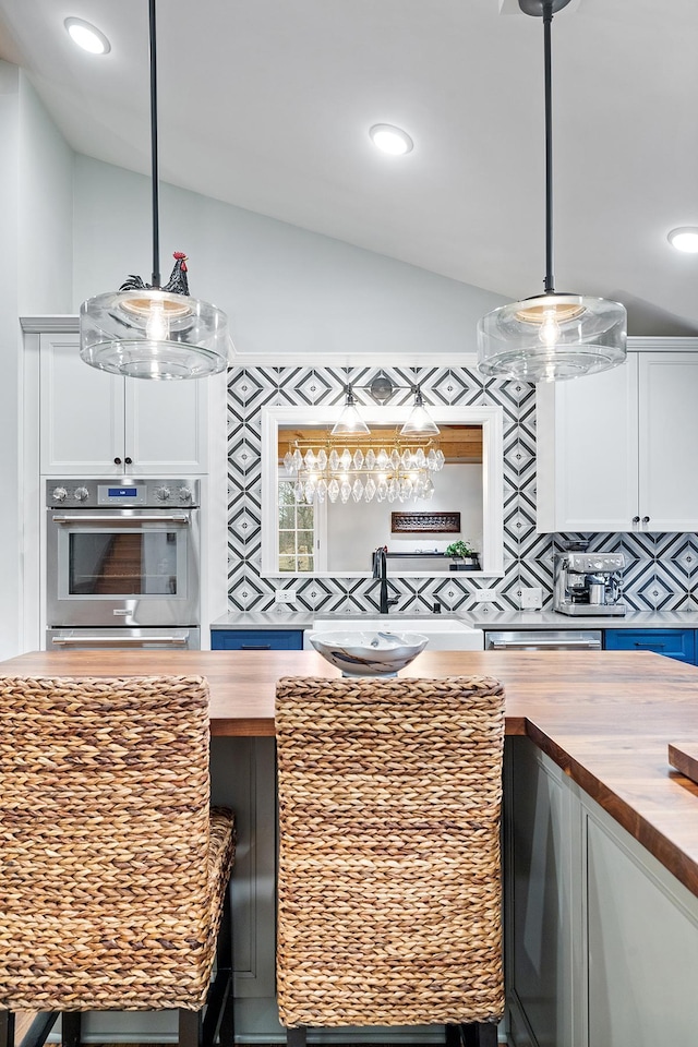 kitchen featuring lofted ceiling, butcher block counters, hanging light fixtures, decorative backsplash, and white cabinetry