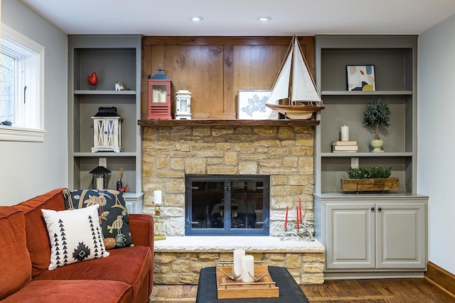 living area featuring built in shelves, baseboards, a fireplace, and wood finished floors