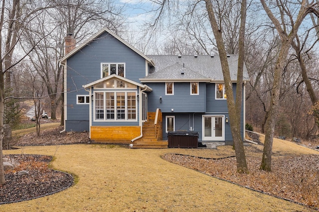 back of property with a sunroom, a hot tub, a chimney, and roof with shingles