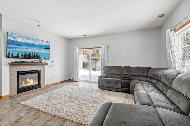 living room with a textured ceiling, a glass covered fireplace, visible vents, and a healthy amount of sunlight