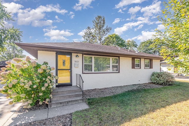 single story home with a shingled roof, a front yard, and stucco siding