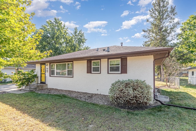 view of property exterior with a shingled roof, a lawn, fence, and stucco siding