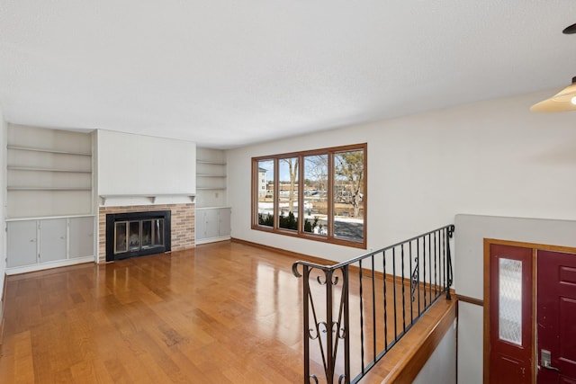 unfurnished living room with baseboards, built in features, stairs, a fireplace, and wood finished floors