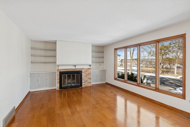 unfurnished living room with visible vents, a brick fireplace, baseboards, wood finished floors, and a textured ceiling