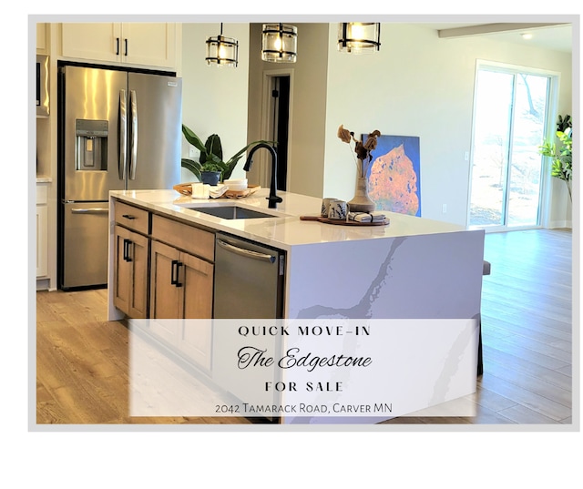 kitchen featuring appliances with stainless steel finishes, light stone counters, a kitchen island with sink, light wood-type flooring, and a sink