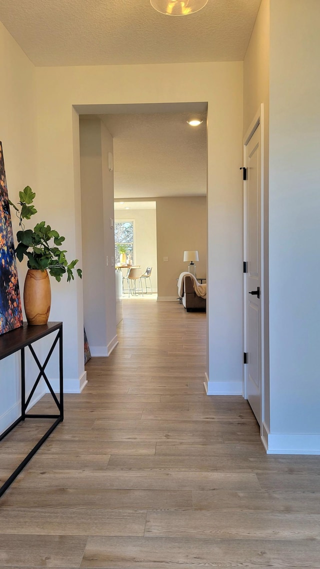 hall featuring a textured ceiling, light wood-type flooring, and baseboards