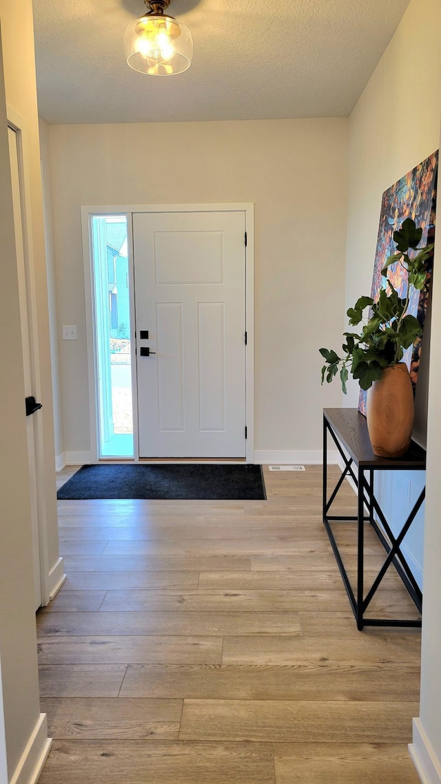 foyer featuring a textured ceiling, light wood-type flooring, and baseboards