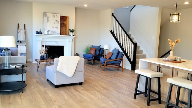 living area with a fireplace, light wood finished floors, recessed lighting, baseboards, and stairs