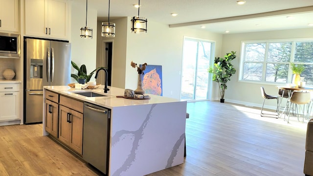 kitchen featuring beam ceiling, appliances with stainless steel finishes, light wood-style floors, a sink, and light stone countertops