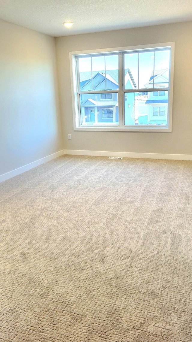 spare room featuring a textured ceiling, carpet floors, visible vents, and baseboards