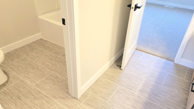 interior space featuring toilet, a bathtub, and baseboards