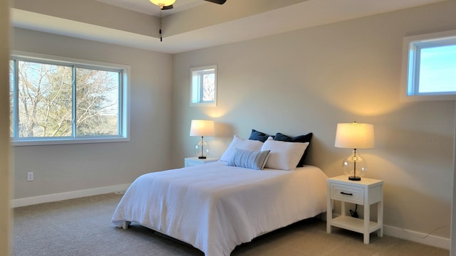 bedroom featuring baseboards, ceiling fan, a tray ceiling, and light colored carpet