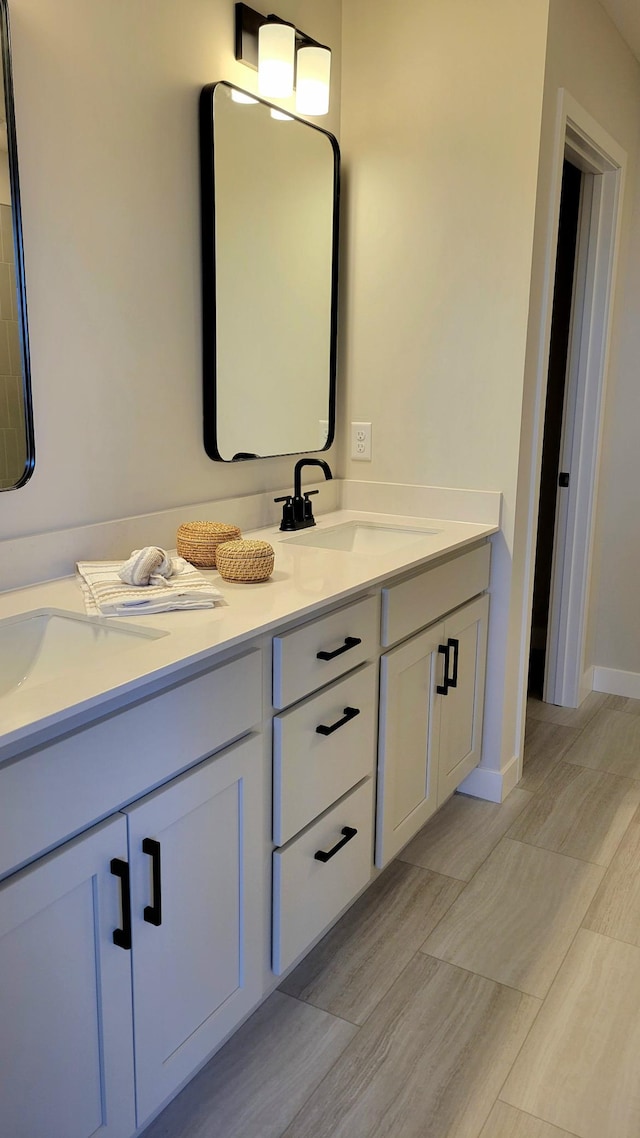 full bath with double vanity, a sink, and baseboards