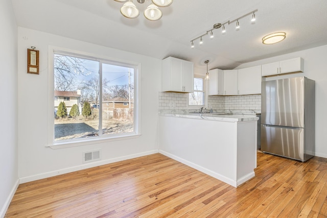 kitchen with visible vents, white cabinetry, light countertops, freestanding refrigerator, and decorative backsplash