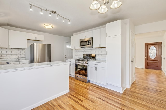 kitchen featuring light wood-style flooring, appliances with stainless steel finishes, white cabinets, and decorative backsplash