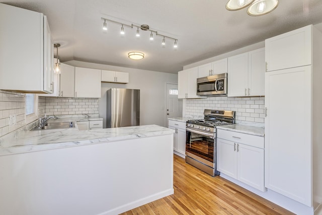 kitchen with appliances with stainless steel finishes, white cabinets, a sink, light wood-type flooring, and a peninsula