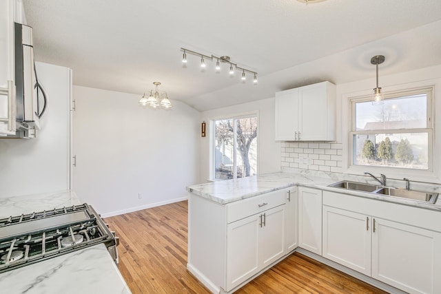 kitchen with lofted ceiling, a peninsula, a sink, stainless steel gas range, and decorative backsplash