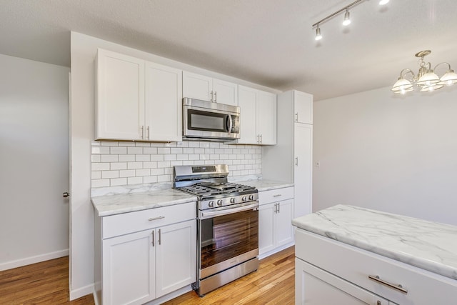 kitchen featuring tasteful backsplash, appliances with stainless steel finishes, light stone countertops, light wood-type flooring, and white cabinetry