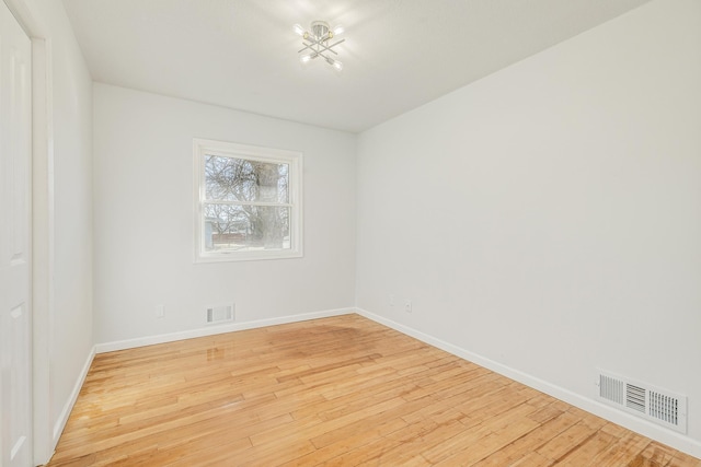 spare room featuring light wood-type flooring, visible vents, and baseboards