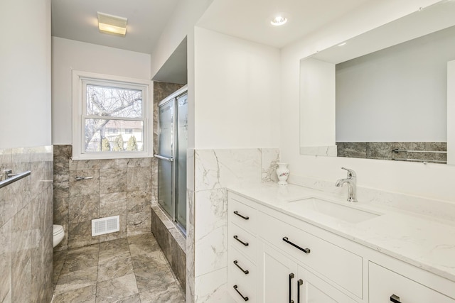 full bathroom with visible vents, a tile shower, tile walls, and vanity