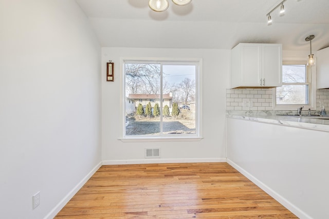 kitchen with light wood finished floors, visible vents, baseboards, white cabinetry, and backsplash