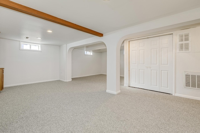 basement with carpet floors, visible vents, arched walkways, and baseboards