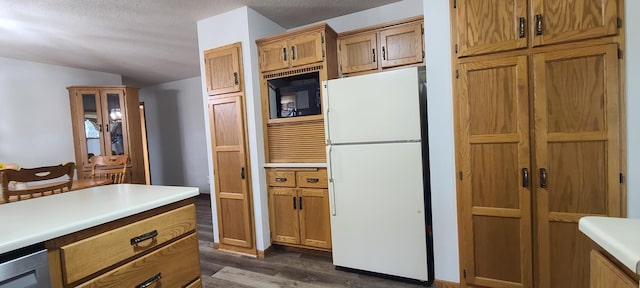 kitchen featuring freestanding refrigerator, brown cabinetry, light countertops, black microwave, and dark wood-style flooring