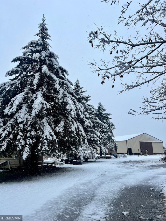 yard layered in snow featuring a detached garage, an outbuilding, and an outdoor structure