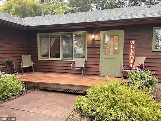 property entrance with roof with shingles and a wooden deck