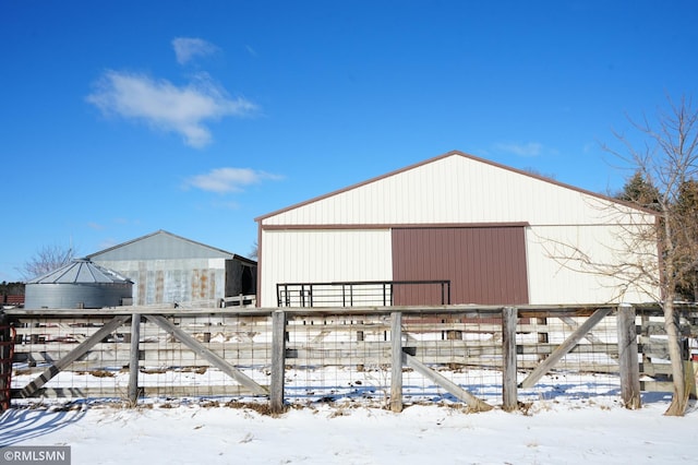 snow covered structure with an outbuilding and fence