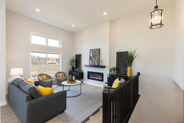 living room featuring baseboards, a glass covered fireplace, light wood-style flooring, an inviting chandelier, and recessed lighting