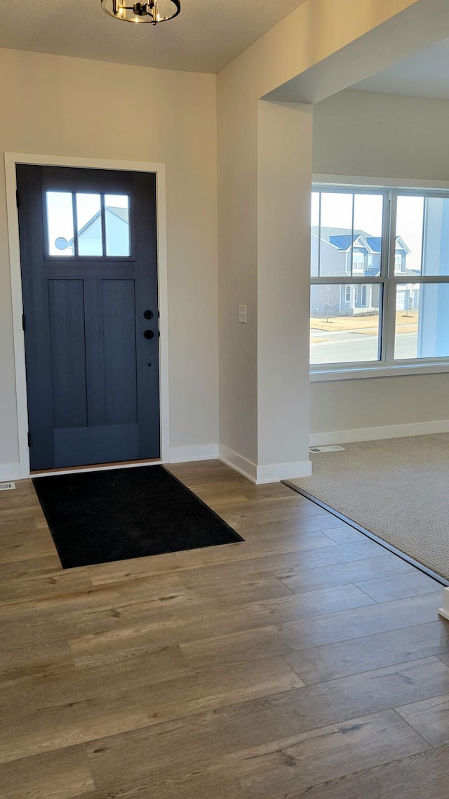 foyer with plenty of natural light, visible vents, baseboards, and wood finished floors