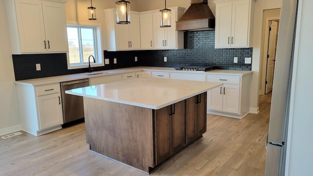 kitchen featuring light wood finished floors, custom range hood, appliances with stainless steel finishes, and a sink