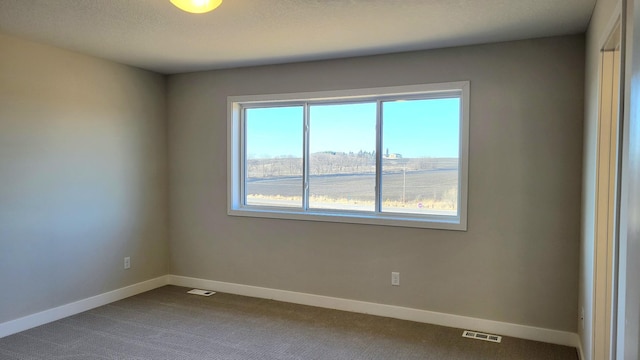 empty room with dark colored carpet, visible vents, and baseboards