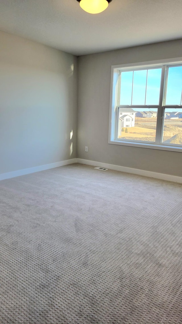 carpeted empty room with visible vents, baseboards, and a wealth of natural light