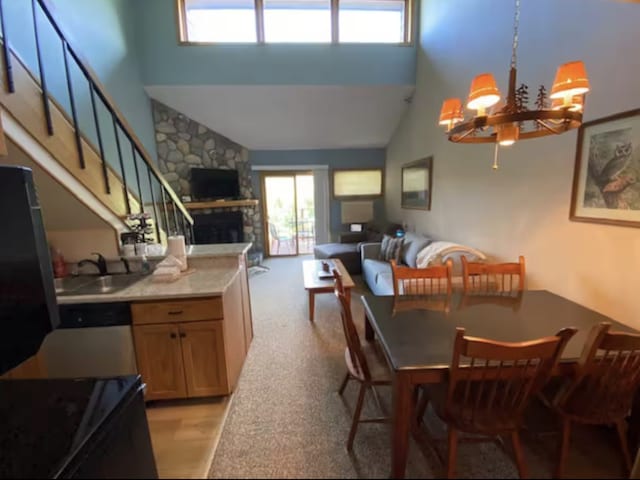 dining space with light carpet, a towering ceiling, stairway, an inviting chandelier, and a fireplace