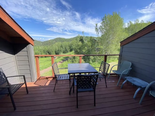 deck with outdoor dining space and a view of trees