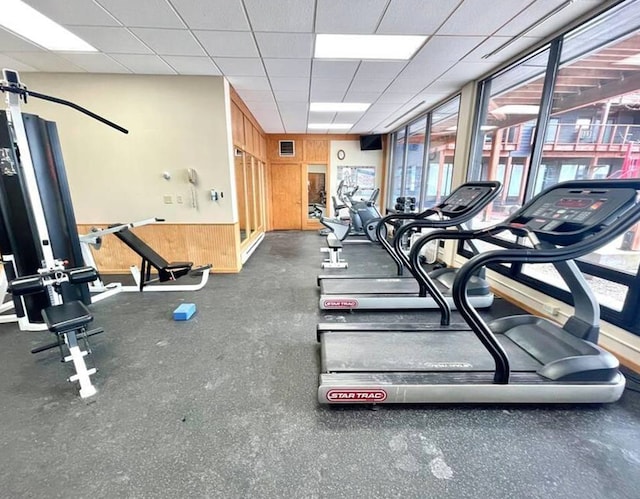 exercise room featuring a paneled ceiling and wooden walls