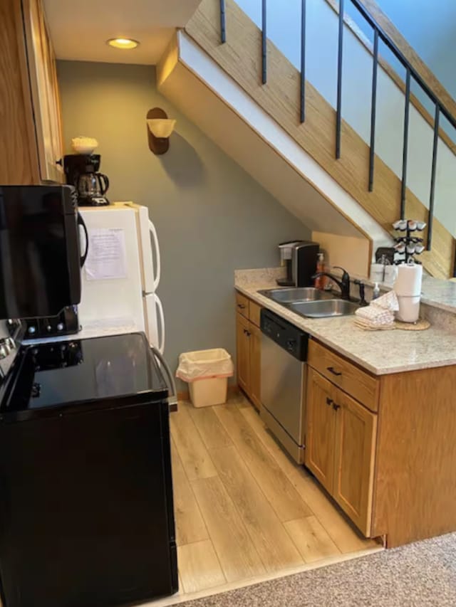 kitchen featuring brown cabinetry, dishwasher, freestanding refrigerator, light wood-style floors, and a sink