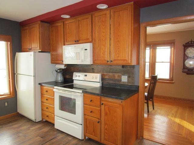 kitchen with dark countertops, white appliances, brown cabinetry, and decorative backsplash