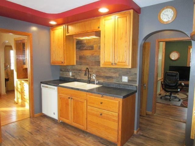 kitchen featuring dishwasher, arched walkways, a sink, and dark wood finished floors