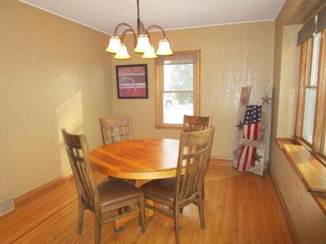 dining area with light wood-type flooring, an inviting chandelier, visible vents, and baseboards