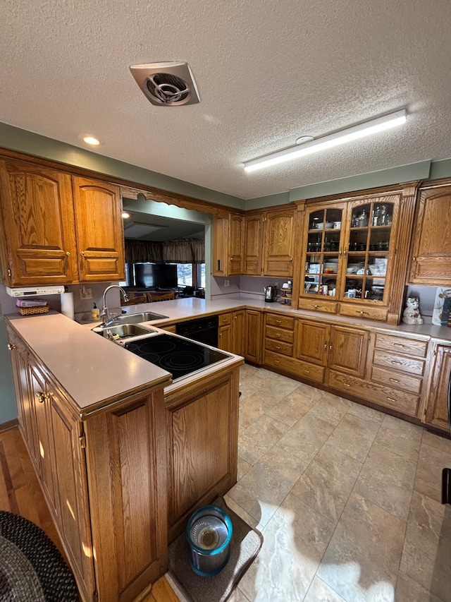 kitchen with brown cabinetry, glass insert cabinets, a sink, and a peninsula