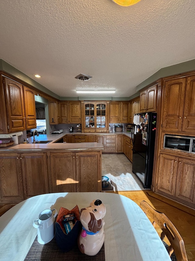 kitchen with visible vents, brown cabinetry, freestanding refrigerator, glass insert cabinets, and a peninsula