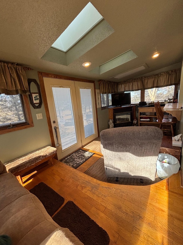 living room featuring a textured ceiling, a skylight, a glass covered fireplace, and hardwood / wood-style flooring